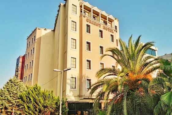 En hotellbyggnad med flera våningar. Det finns palmer och gröna träd framför byggnaden. (AI-genererad text)