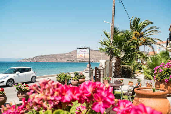 En kuststräcka med blått hav, blommor i förgrunden och en vit bil parkerad vid sidan. (AI-genererad text)