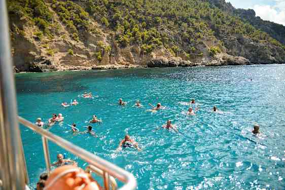 Badande människor i klart blått vatten framför en klippig kustlinje. (AI-genererad text)