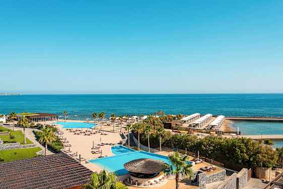 Utsikt över en resort med pool, solsängar, palmer och hav i bakgrunden. (AI-genererad text)