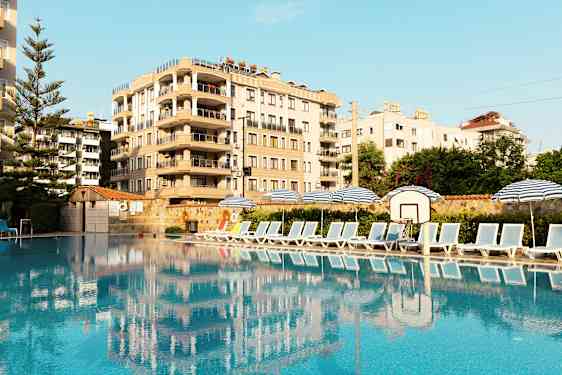 Bild av en pool med solstolar och parasoller vid sidan, samt en byggnad i bakgrunden. (AI-genererad text)