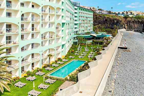 Ett hotell med flera våningar vid havet, gräsmatta med solstolar och pool utanför. (AI-genererad text)