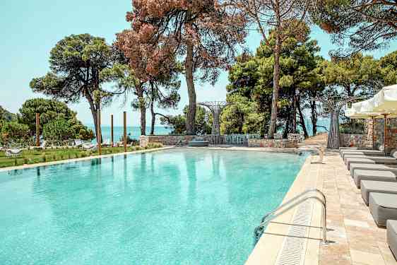 Utomhuspool omgiven av solstolar, grönska och havsutsikt. (AI-genererad text)