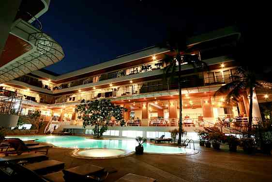 Kvällsvy av en byggnad med flera våningar, lysande fasad och en pool i förgrunden. (AI-genererad text)