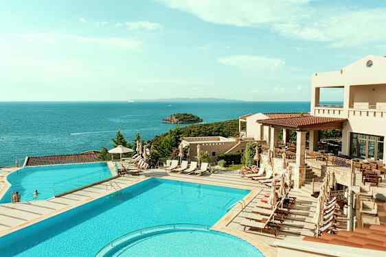 Vy över en poolområde med solstolar och havet i bakgrunden. (AI-genererad text)