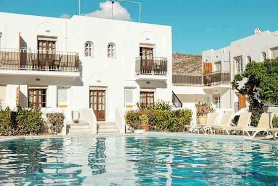 Vit byggnad med pool och solstolar framför. (AI-genererad text)