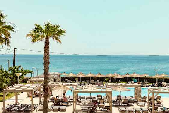 En vy över utomhuspoolområde med solstolar, parasoller, och havet i bakgrunden. (AI-genererad text)