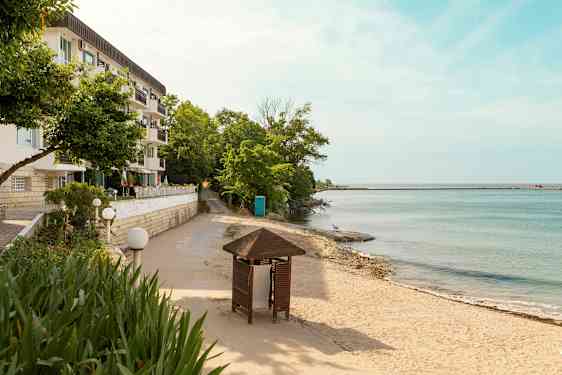 En byggnad med flera balkonger bredvid en sandstrand och hav med träd och en paviljong i förgrunden. (AI-genererad text)