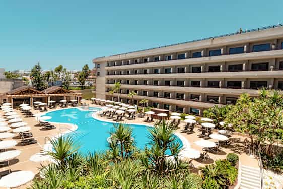 En hotellbyggnad med balkonger och en pool omgiven av solstolar och parasoller. (AI-genererad text)