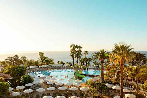 En utomhuspool med solstolar omgivna av palmer och utsikt över havet. (AI-genererad text)