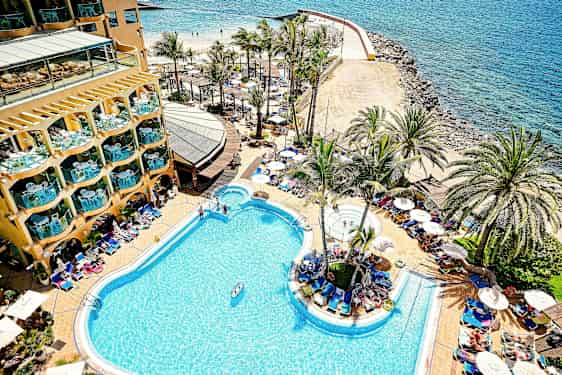 En hotellpool vid kusten med palmer och solstolar runt omkring. (AI-genererad text)