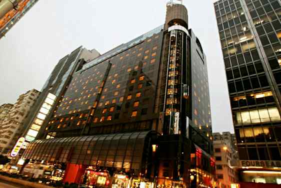 Ett upplyst flervåningshus i en stadsmiljö med glasfasad och gatuliv i förgrunden. (AI-genererad text)