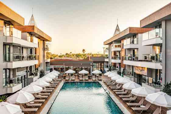 Hotellområde med pool och solsängar omgivna av byggnader. (AI-genererad text)