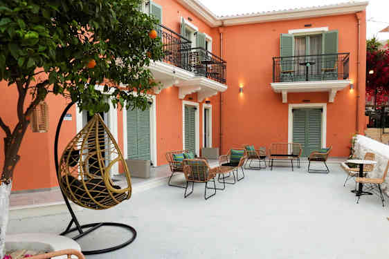 En uteplats med stolar och bord framför en byggnad med orange fasad och gröna fönsterluckor. (AI-genererad text)