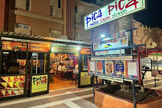 En restaurang med namnet Pica Pica visas på natten. Skyltar och menyer pryder exteriören. (AI-genererad text)
