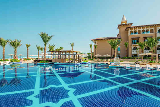 En swimmingpool med solstolar vid kanten, omgiven av palmer och en byggnad i bakgrunden. (AI-genererad text)