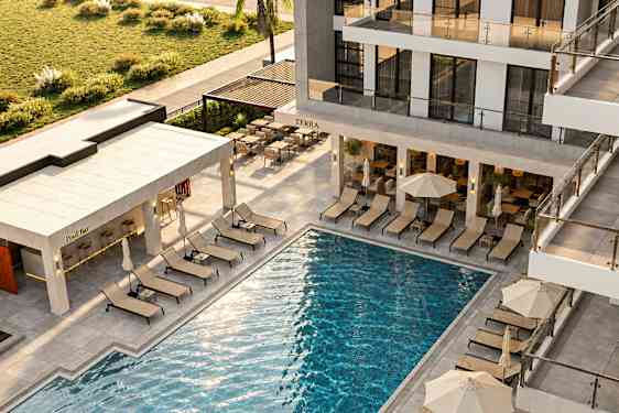 Vy över en modern anläggning med pool, omgivet av solstolar och parasoller. En poolbar ligger i anslutning. (AI-genererad text)