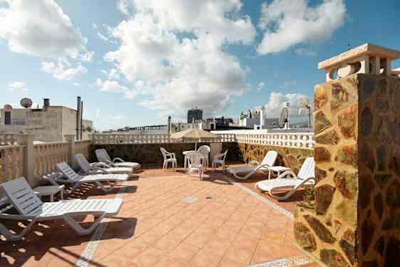 Solstolar och ett bord med stolar på en terrass med utsikt över byggnader. (AI-genererad text)