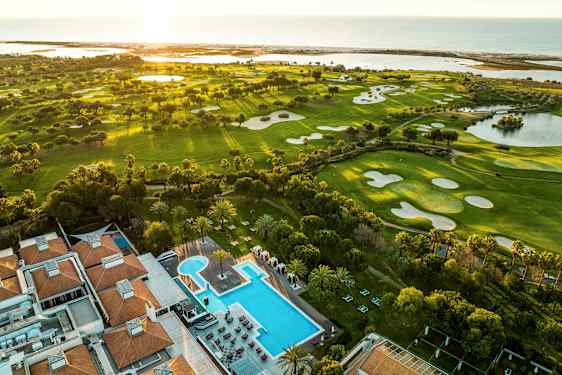 Flygfoto över golfbanor och ett hotell med poolområde. (AI-genererad text)