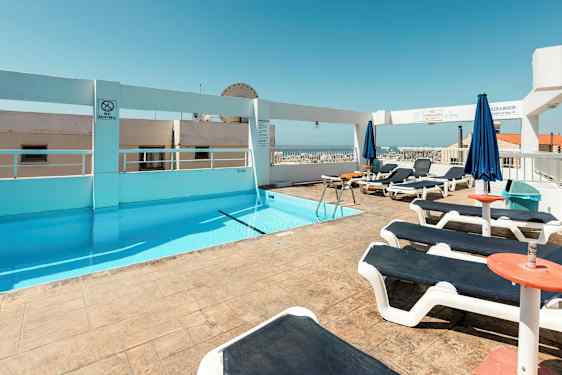 En takterrass med en pool och solstolar under en klar blå himmel. (AI-genererad text)