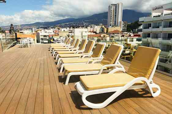 En takterrass med solstolar och utsikt över en stad och omgivande berg. (AI-genererad text)