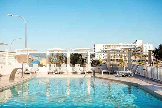 Utomhuspool med solstolar och parasoller, i bakgrunden syns byggnader och havet. (AI-genererad text)