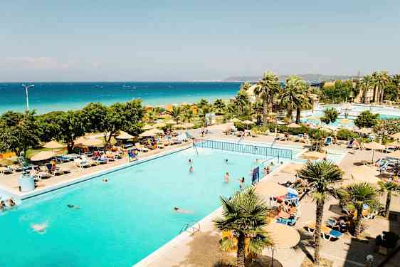 En utomhuspool omgiven av solstolar och parasoller, med palmer och hav i bakgrunden. (AI-genererad text)