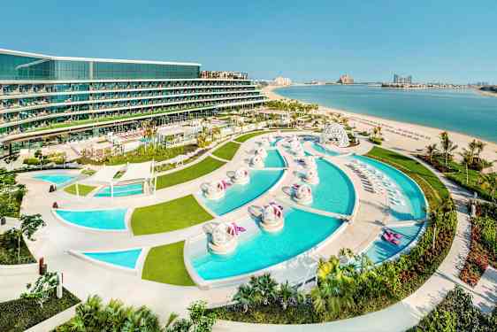 Vy över en resort med flera pooler, grönområden och en sandstrand vid havet. (AI-genererad text)