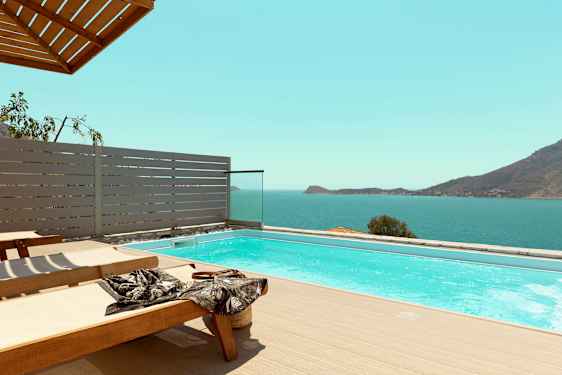 Solstolar vid en pool med utsikt över havet och berg. (AI-genererad text)