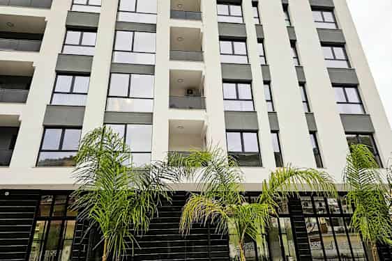 Flerbostadshus med glasfasad och balkonger, omgiven av palmer. (AI-genererad text)