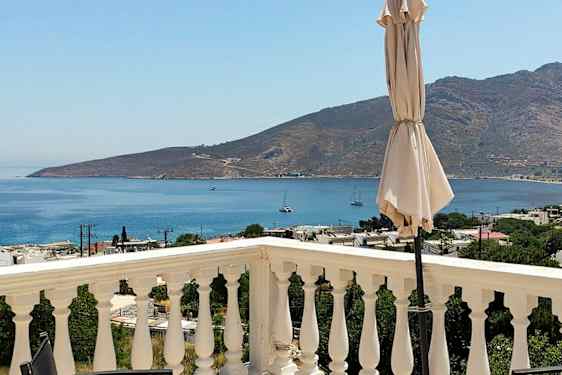 En vy från en terrass med räcken, en parasoll och en utsikt över havet och berg i bakgrunden. (AI-genererad text)