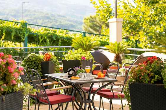 Bord med rödklädda stolar omgivna av grönska och färgglada blommor. (AI-genererad text)