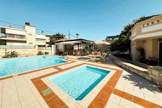 Två utomhuspooler omgivna av solstolar och ett skuggaområde med färgglada stolar. (AI-genererad text)