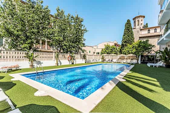 Utomhuspool med solstolar runtom, omgivande byarkitektur och grönska. (AI-genererad text)