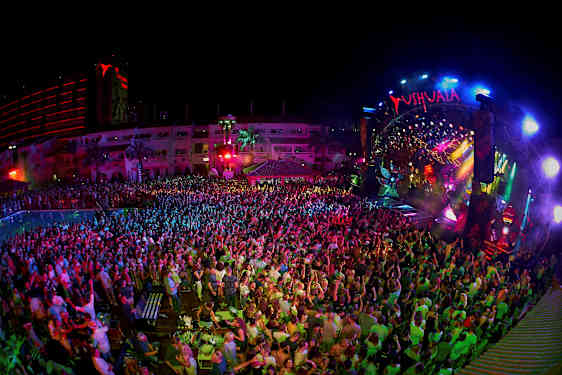 En nattklubb med ett publikhav framför en färgglatt lysande scen. (AI-genererad text)