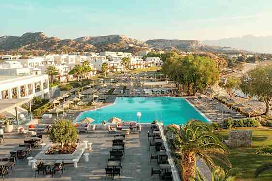 Luftbild av en semesteranläggning med pool, solstolar, byggnader och omgivande landskap. (AI-genererad text)