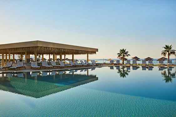 En utomhuspool med solstolar och parasoller vid havet. (AI-genererad text)