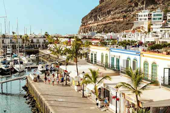 Bild av en hamn med segelbåtar, omgiven av färgglada byggnader och palmträd. (AI-genererad text)