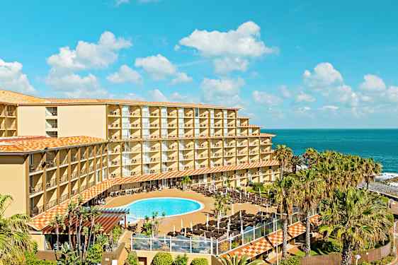 Hotellbyggnad med balkonger, poolområde och hav i bakgrunden. (AI-genererad text)