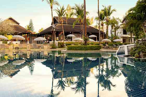 En utomhuspool med solstolar och parasoller vid sidan samt omgivande tropisk vegetation. (AI-genererad text)