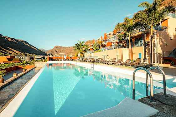 Utomhuspool vid ett hotell med solstolar och berg i bakgrunden. (AI-genererad text)