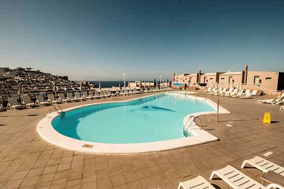 Utsikt över en utomhuspool omgiven av solstolar och parasoller. (AI-genererad text)