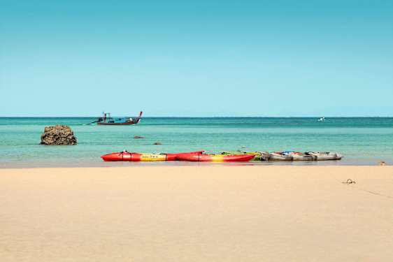 Flera kajaker på en sandstrand, med havet och en båt i bakgrunden. (AI-genererad text)