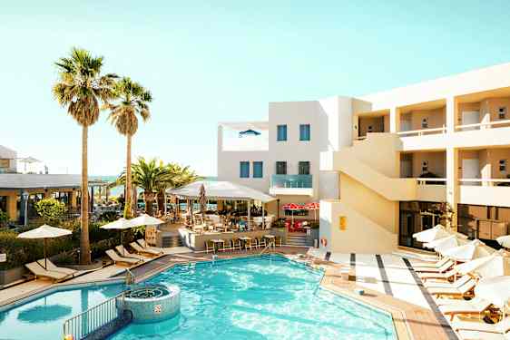 En utomhuspool omgiven av solstolar och parasoller vid ett hotell med beige fasad. (AI-genererad text)