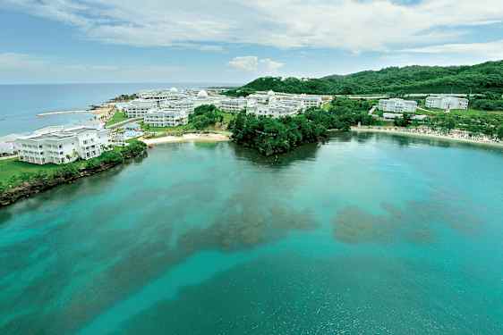 Bild av en kust med klart vatten och vita byggnader omgivna av grönska. (AI-genererad text)