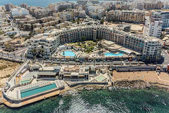 Bilden visar en omfattande semesterresort med pooler, solområden och omgivande byggnader nära kusten. (AI-genererad text)