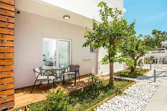 En terrass med trätrall och två stolar kring ett bord, omgiven av växter och ett citrusträd. (AI-genererad text)