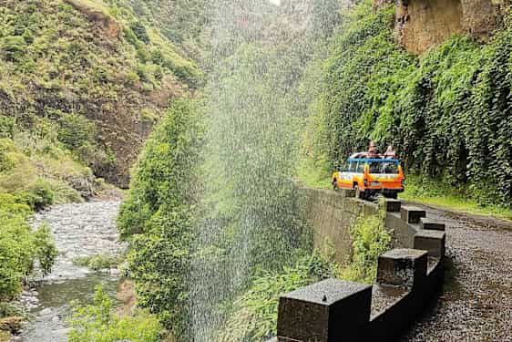 En gul-orange jeep på en väg vid ett vattenfall i en grön dal. (AI-genererad text)