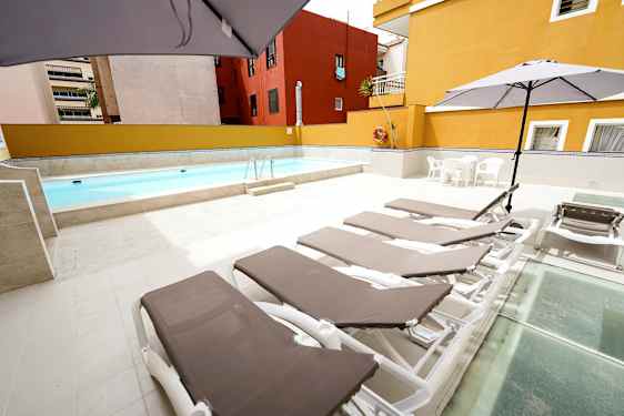 Utomhuspool med solstolar och parasoller på ett stenlagt område. (AI-genererad text)