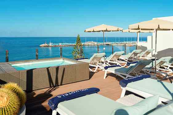 Terrass med solstolar och parasoller vid en jacuzzi med havsutsikt. (AI-genererad text)